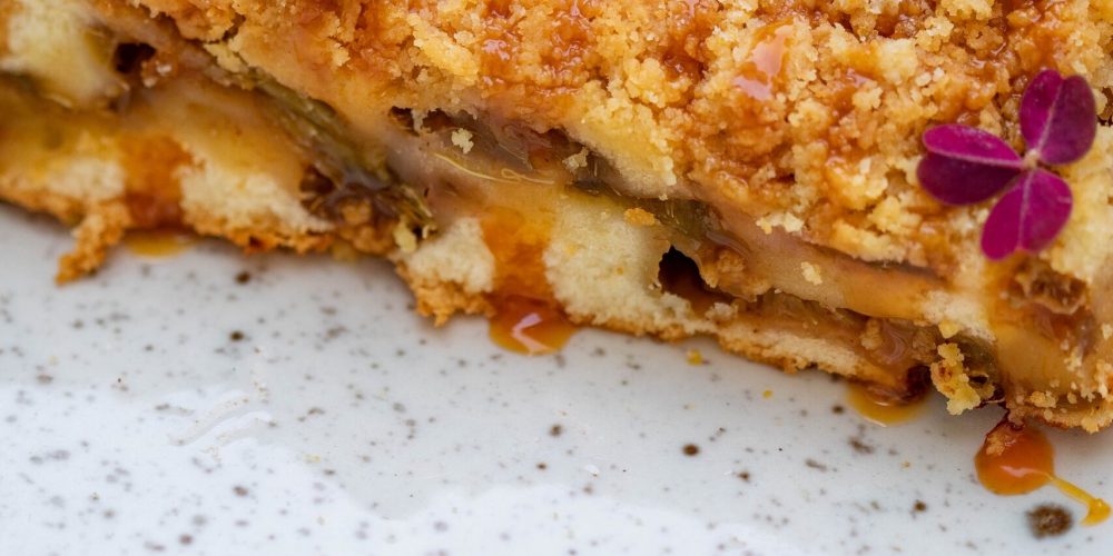 A close-up of apple crisp with a golden oat crumble topping and cream.
