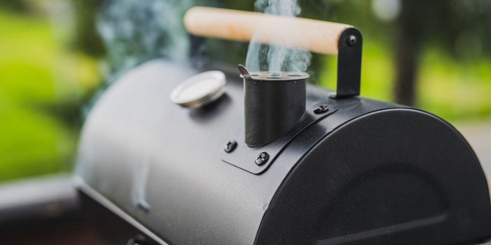 Focus shot on a smoker with steam coming out from it while set outdoors.